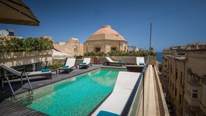 A rooftop pool with lounge chairs and a view of the sea.