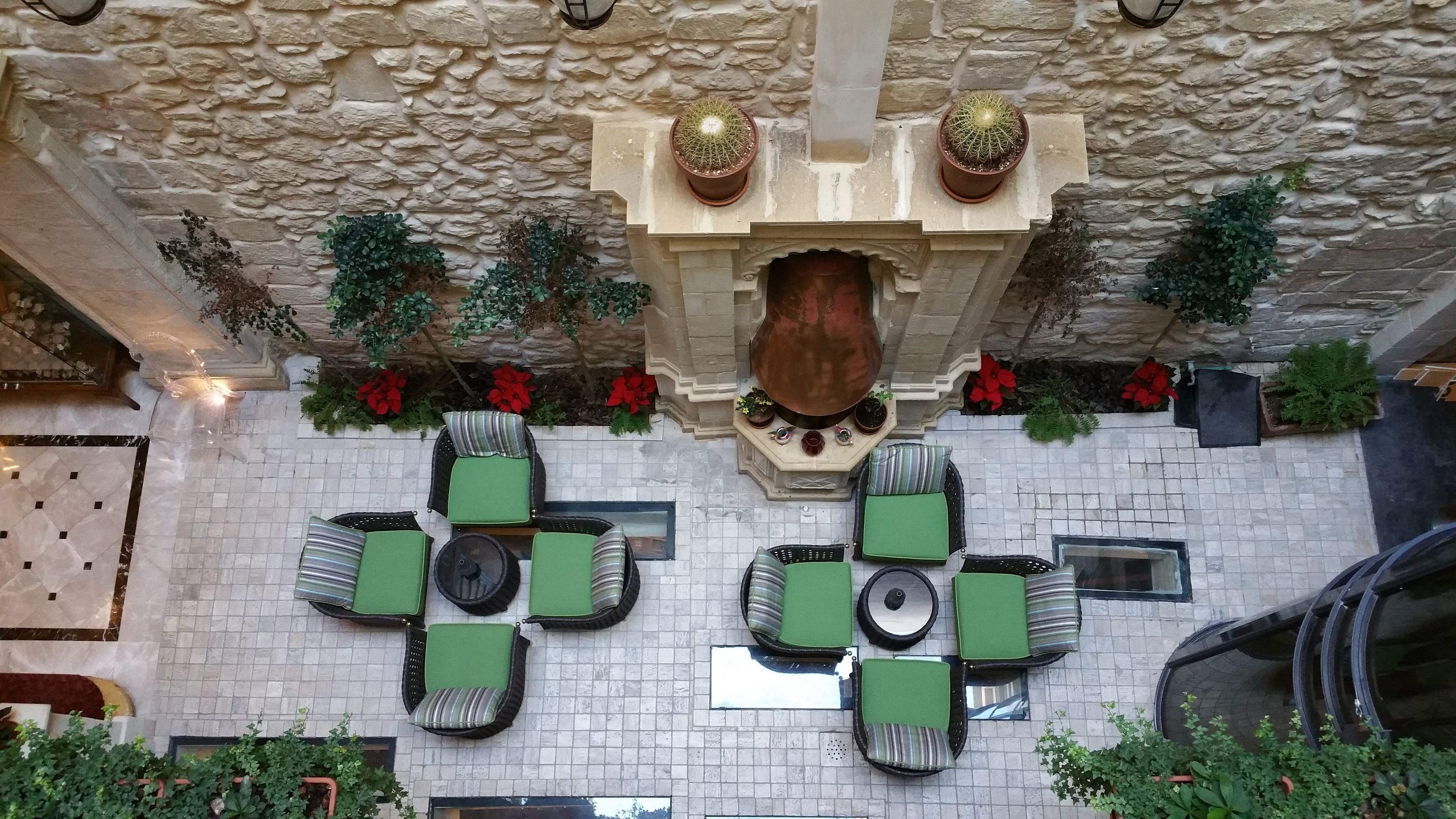 A rooftop terrace with stone walls, green cushioned seating, and potted plants.