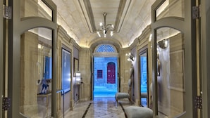 A grand hallway with marble flooring, a chandelier, and a view of a red door at the end.
