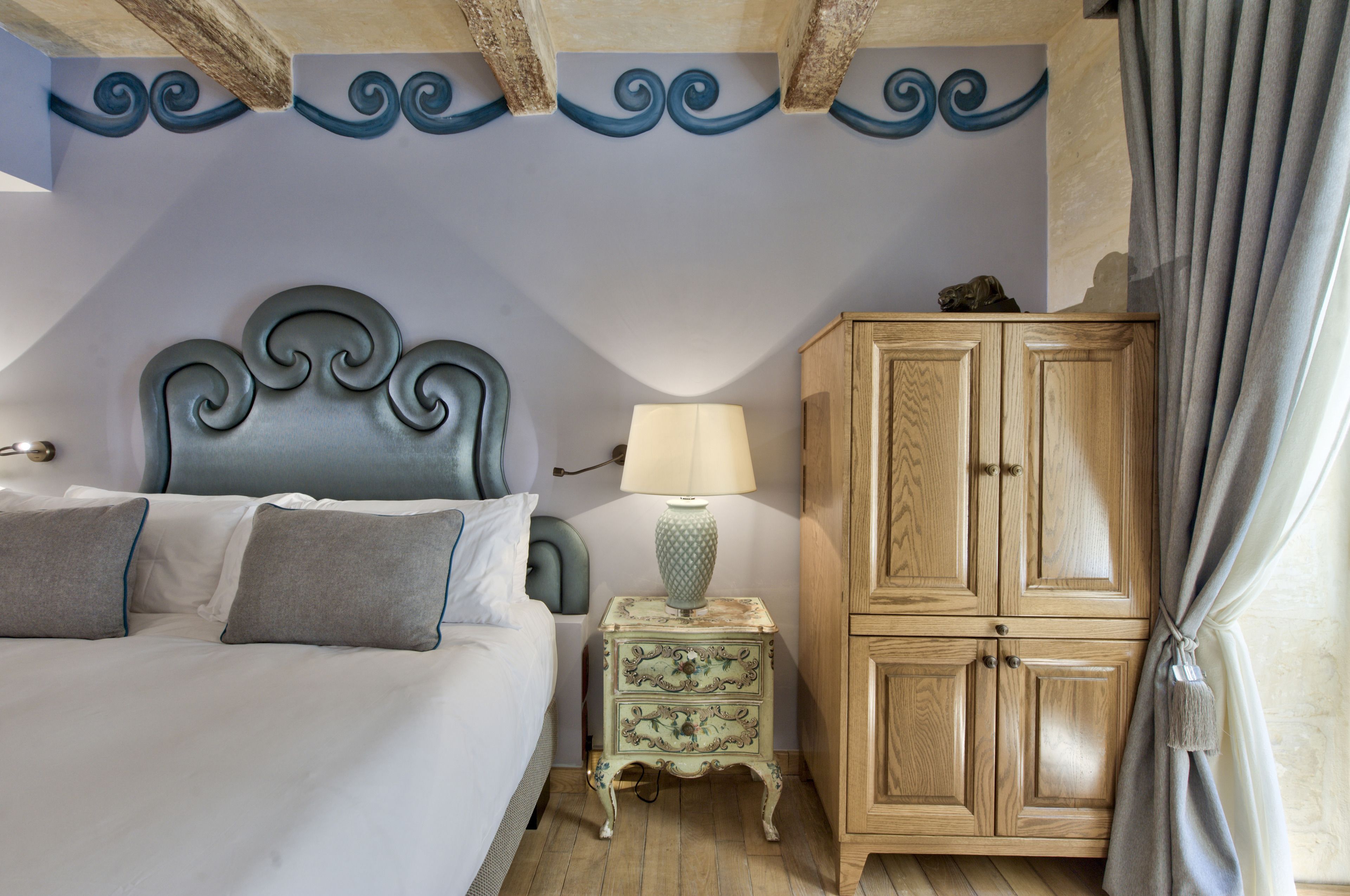 A bedroom with a bed, a nightstand, a lamp, a wooden cabinet, and a curtain.