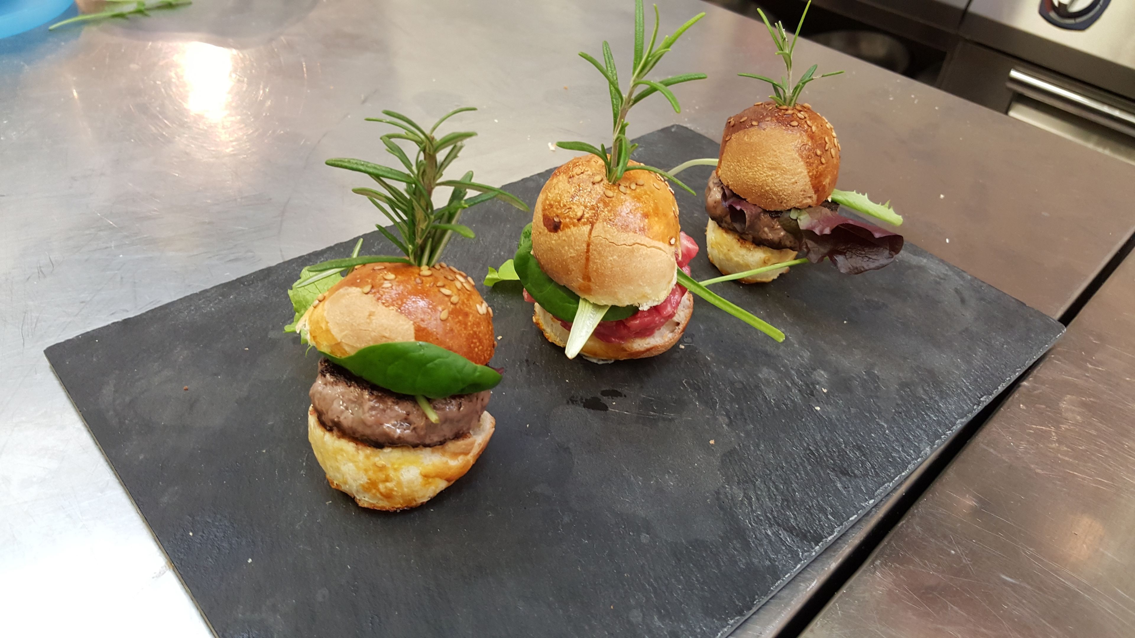 Three gourmet burgers on a black slate plate.