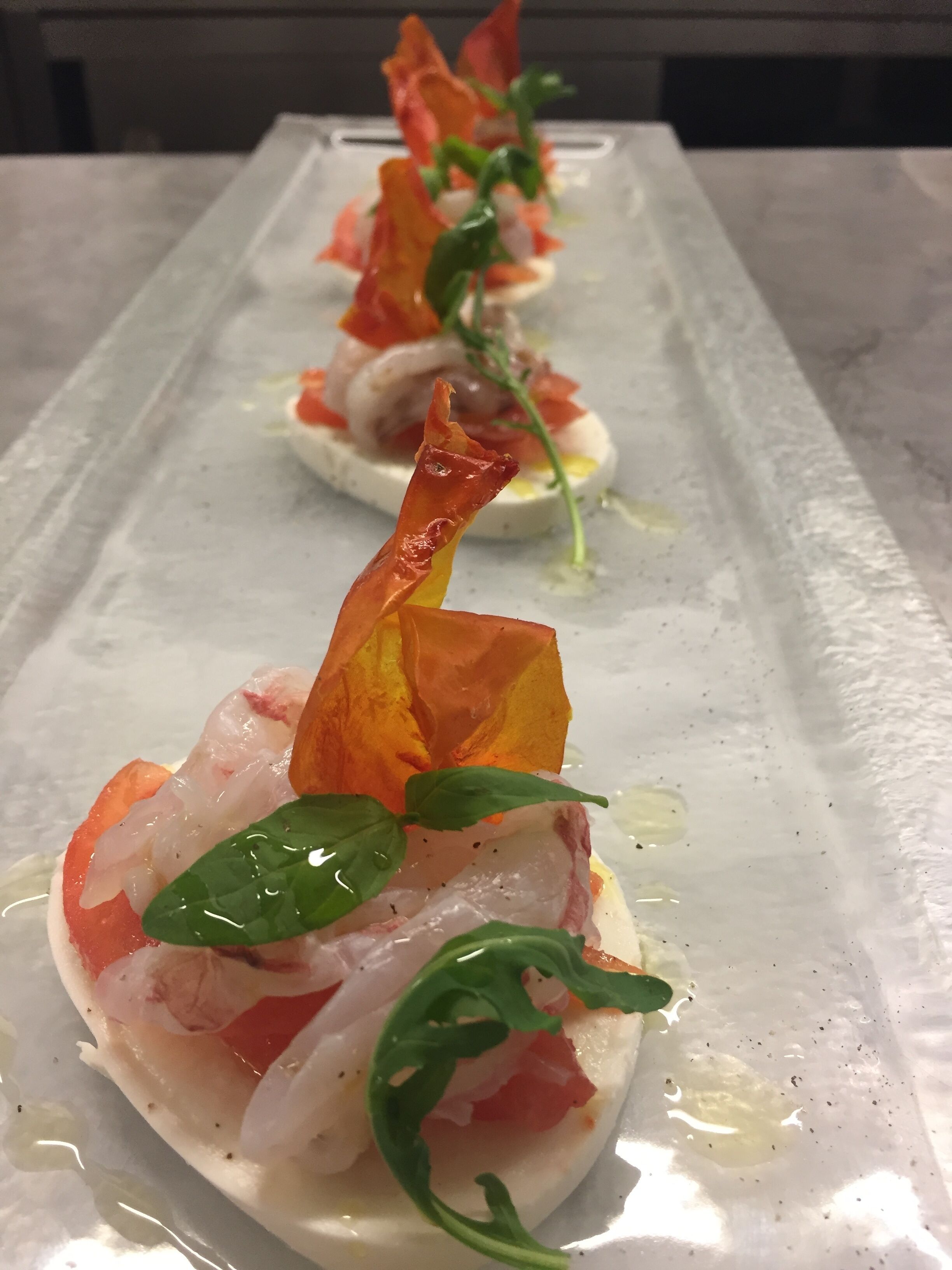 A row of appetizers on a white plate with a clear liquid.