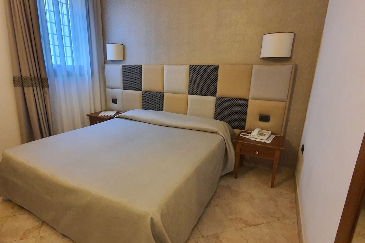 Una habitación de hotel con una cama grande, una mesita de noche con teléfono y un cabecero con lámpara.