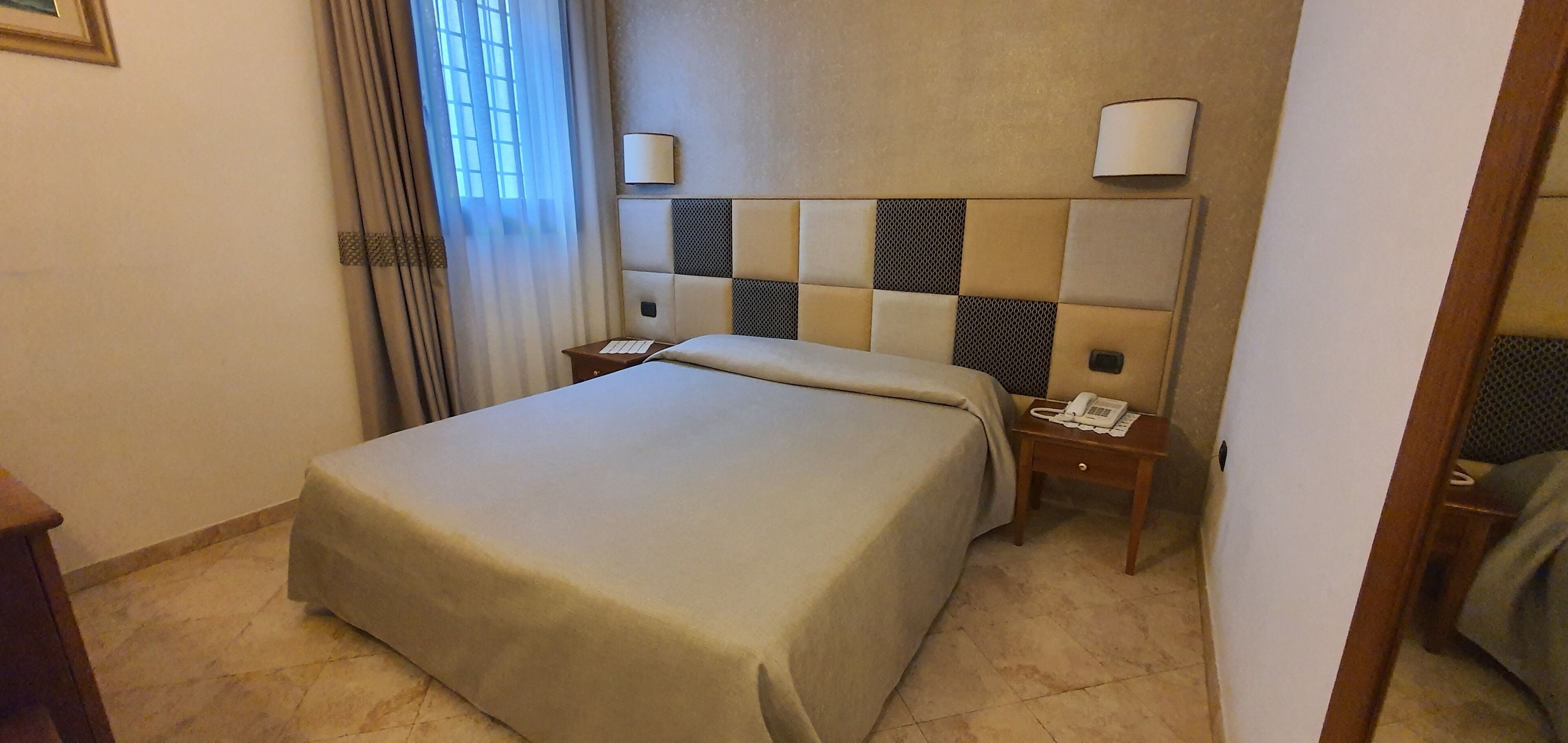 A hotel room with a large bed, a bedside table with a phone, and a headboard with a light fixture.