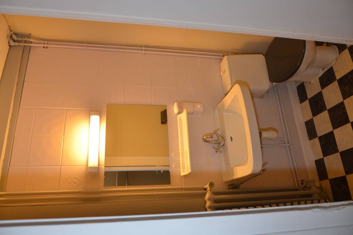 A bathroom with a toilet, sink, and mirror. The floor has a checkered pattern.