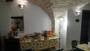 A dining area with a buffet table covered in a floral tablecloth, a stone wall, and a ceiling with exposed brick. - Accogliente Dimora (Putignano)