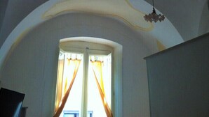 A room with a high arched ceiling, a chandelier, and a window with curtains. - Accogliente Dimora (Putignano)