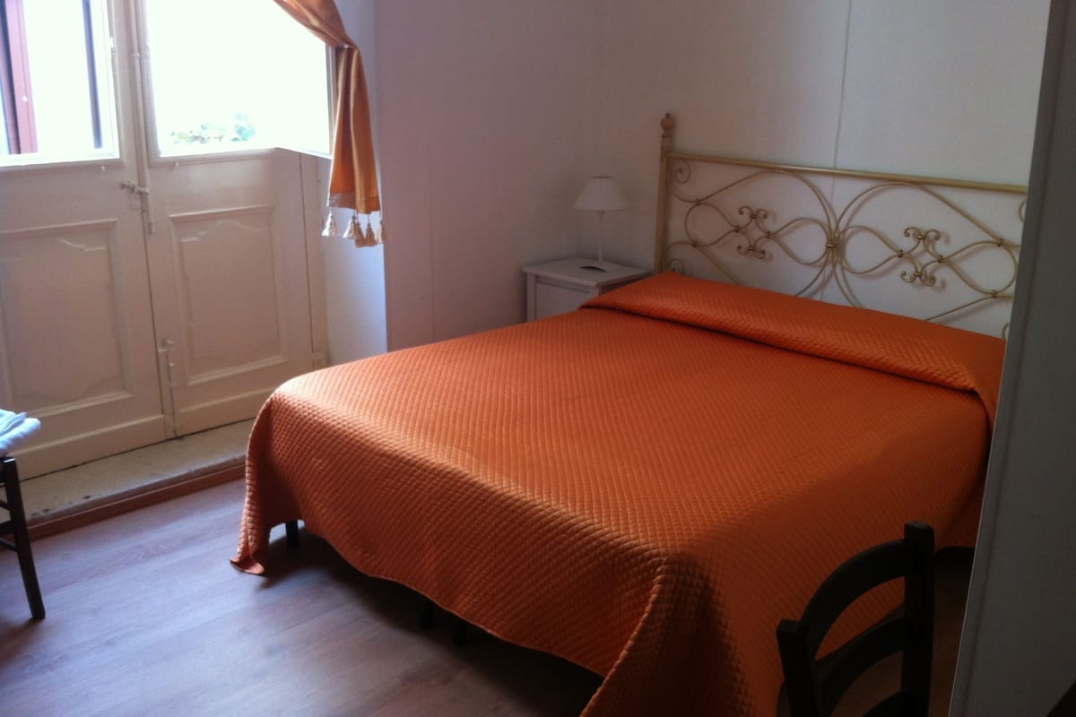 Un dormitorio con una cama, una mesita de noche, una lámpara y una ventana con cortinas.