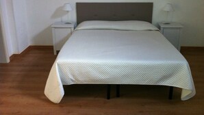 A neatly made bed with a white quilt in a simple room with wooden flooring and white walls. - Accogliente Dimora (Putignano)