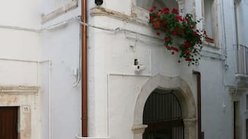 A narrow street with white buildings, a wooden door labeled '15', and a black gate.