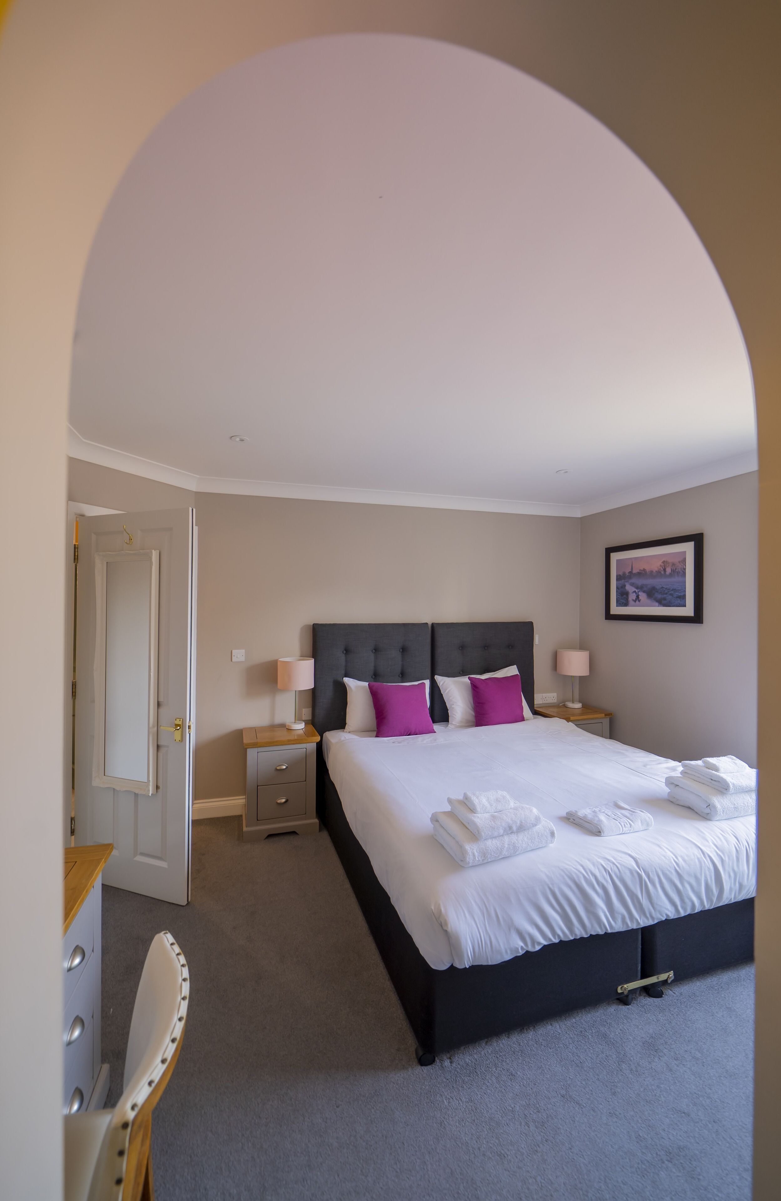 Una camera da letto con un letto grande, due comodini con lampade, una porta e un quadro appeso al muro.