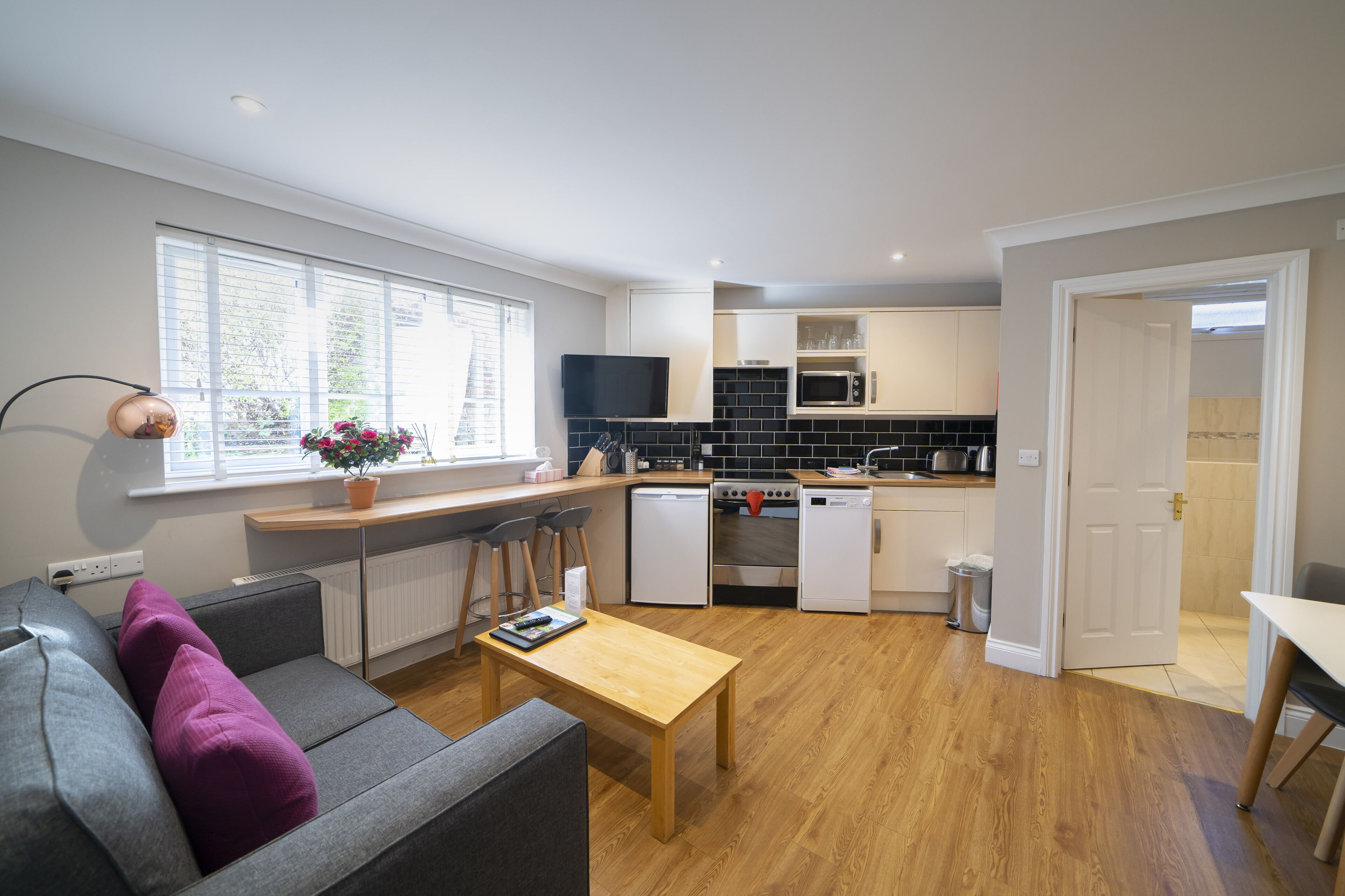 A modern kitchen with a built-in oven, microwave, and dishwasher. There is a dining area with a wooden table and chairs.