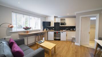 A modern kitchen with a built-in oven, microwave, and dishwasher. There is a dining area with a wooden table and chairs.