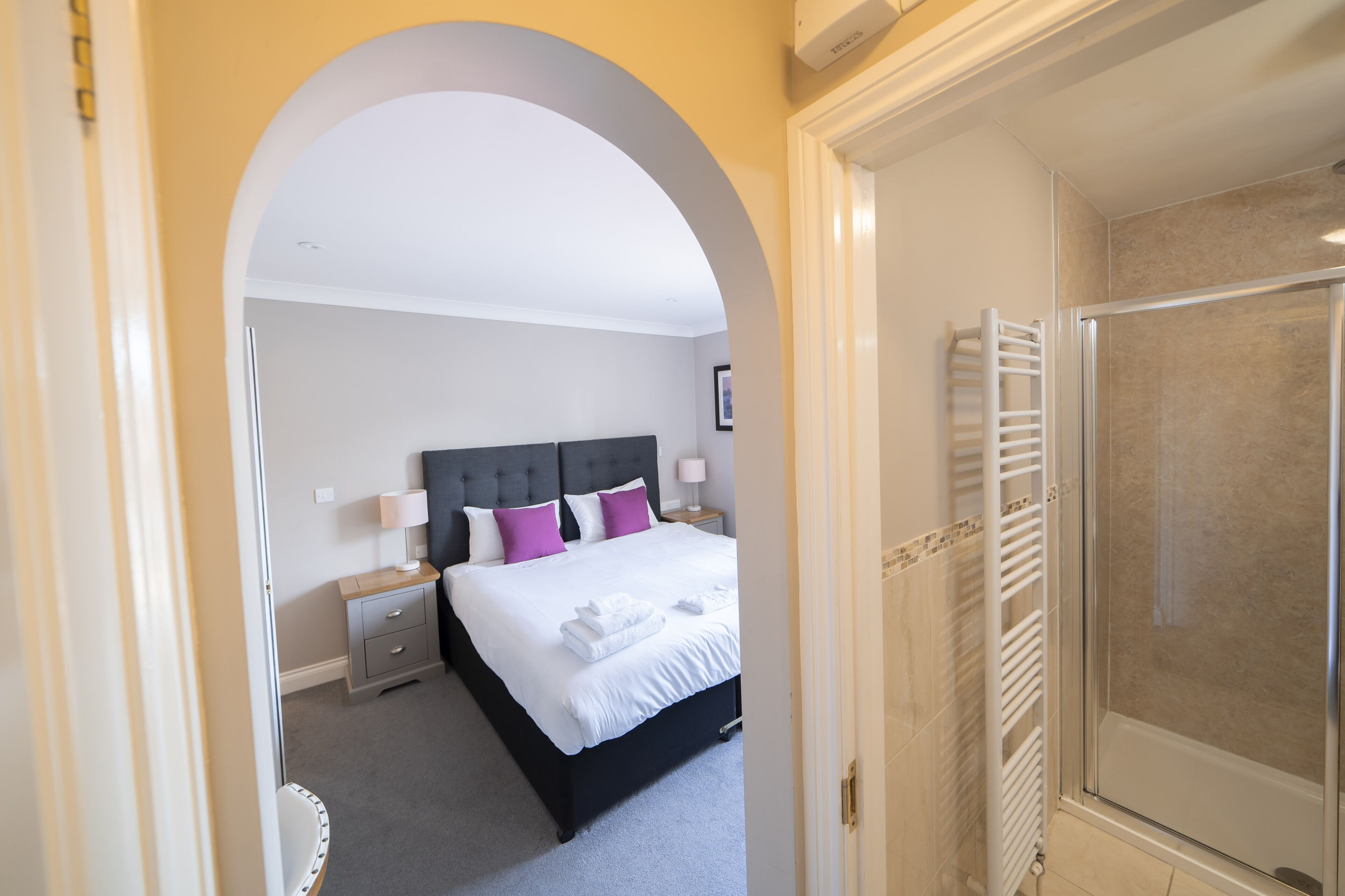 Une chambre d’hôtel comprenant un lit, une table de chevet, une lampe et un espace douche.