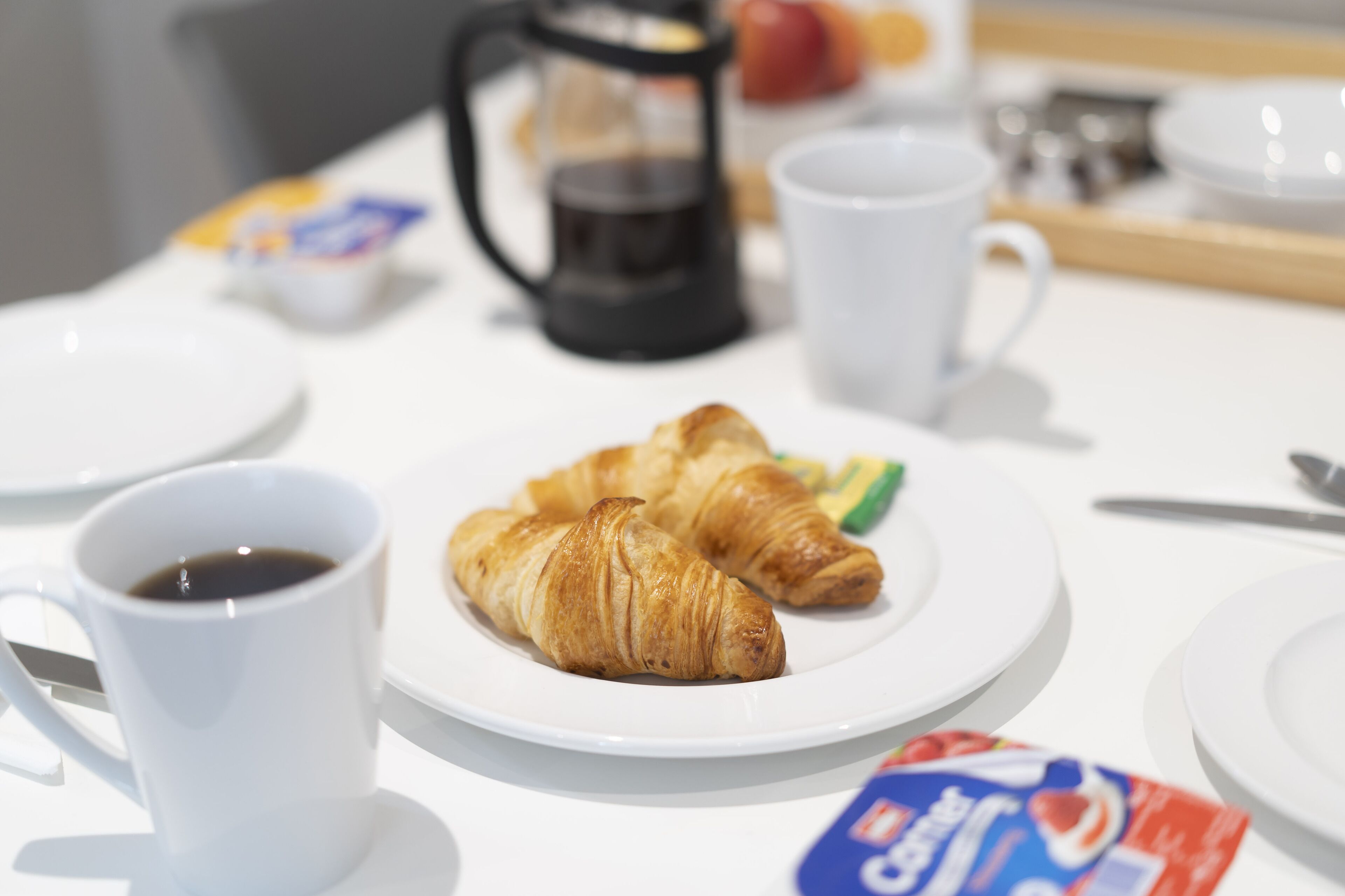 A breakfast table with croissants, a coffee cup, and a packet of cream.