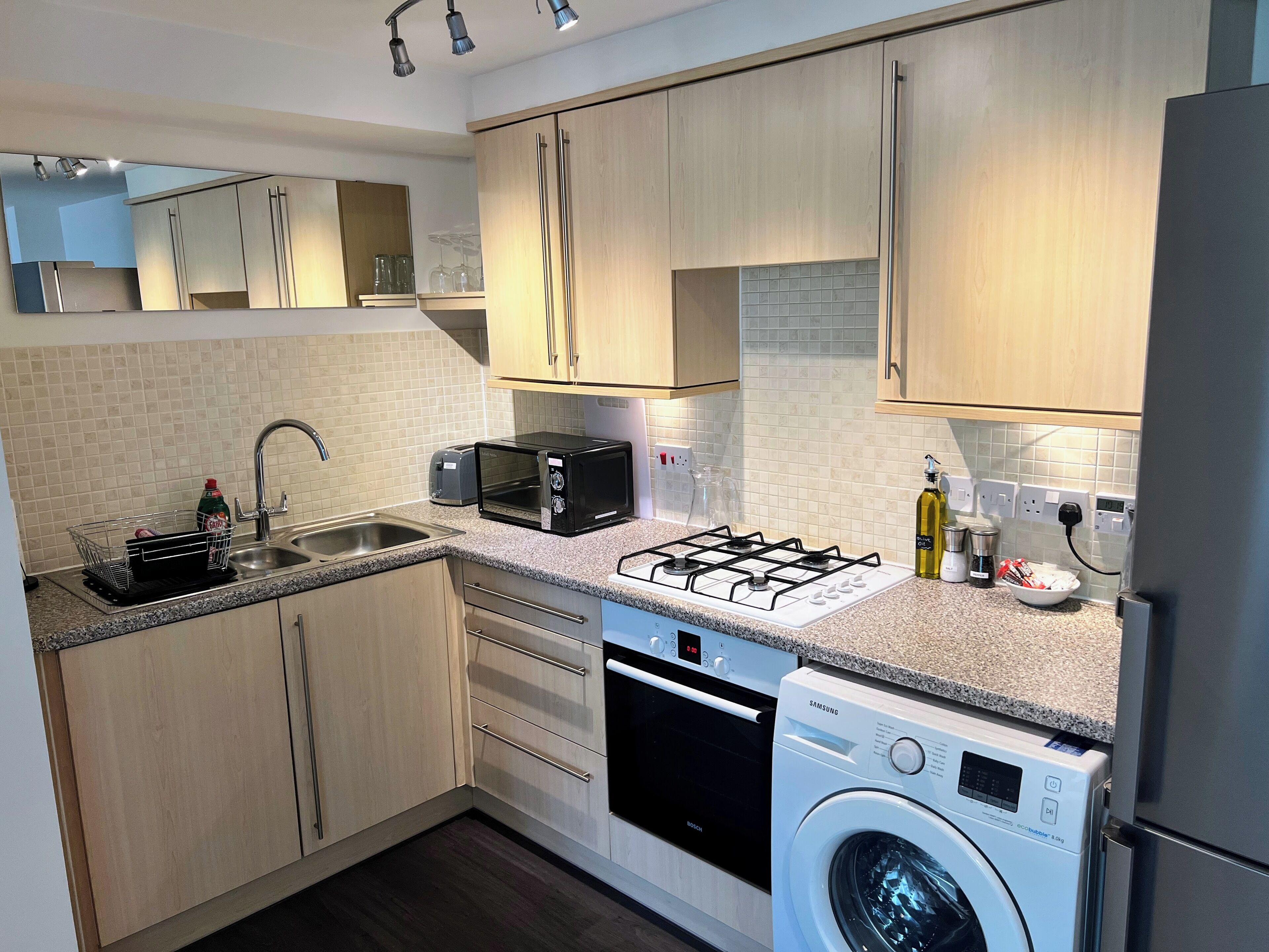 A modern kitchen with wooden cabinets, a gas stove, a microwave, a dishwasher, and a washing machine.