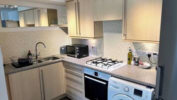 A modern kitchen with wooden cabinets, a gas stove, a microwave, a dishwasher, and a washing machine.