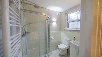 Un baño con ducha de mampara de vidrio, inodoro y lavamanos.