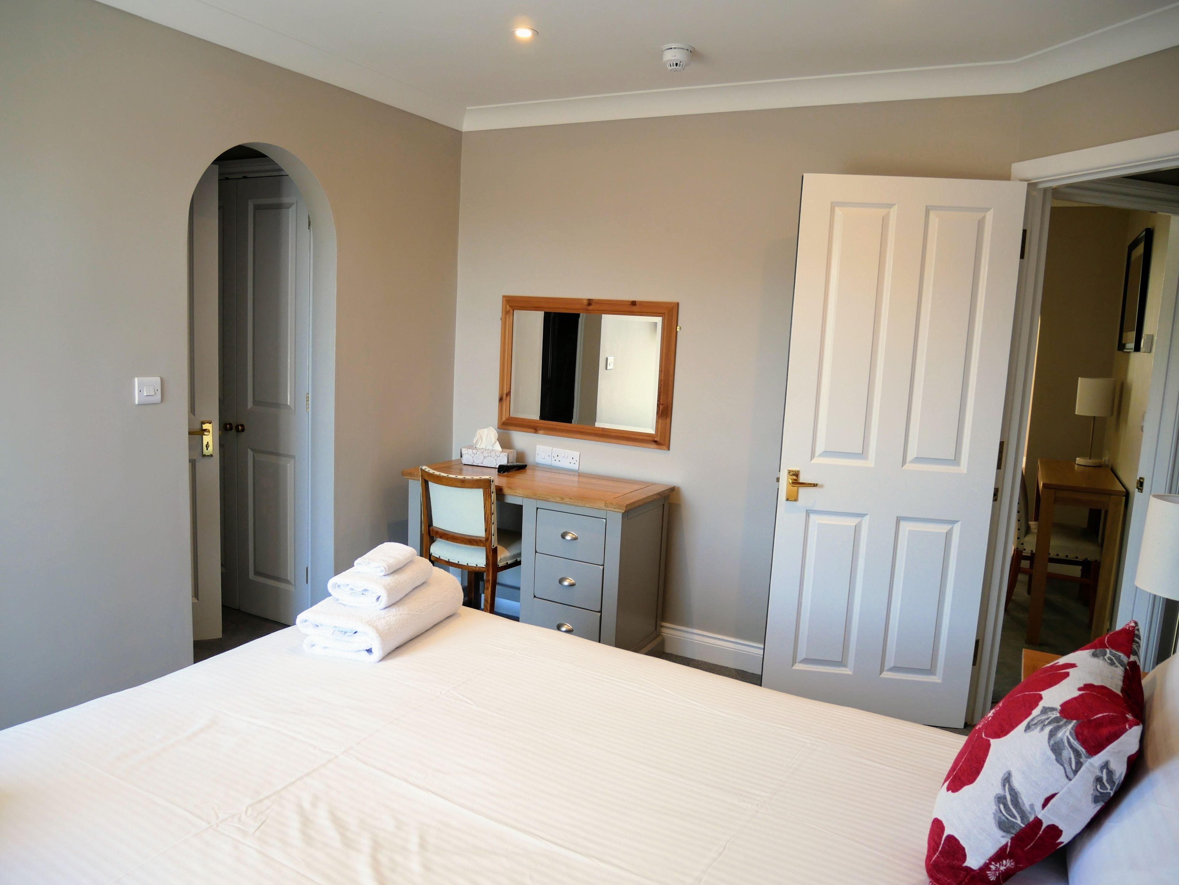 A bedroom with a bed, a desk, a chair, a mirror, and a door.