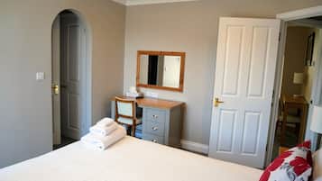 A bedroom with a bed, a desk, a chair, a mirror, and a door.
