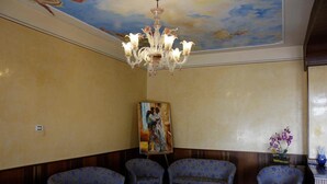Una habitación con cuatro sillones azules estampados con flores, una araña, un cuadro en la pared y un jarrón con flores sobre una mesa.