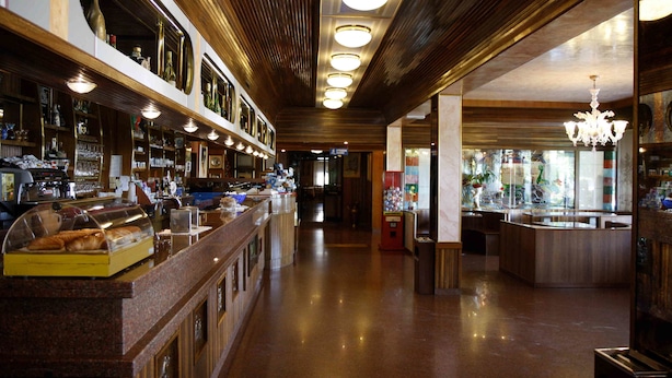 Una zona de bar con una barra larga, estantes con botellas y una vitrina con pasteles.