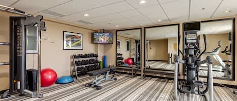 A gym with exercise equipment, a television, and a mirror.