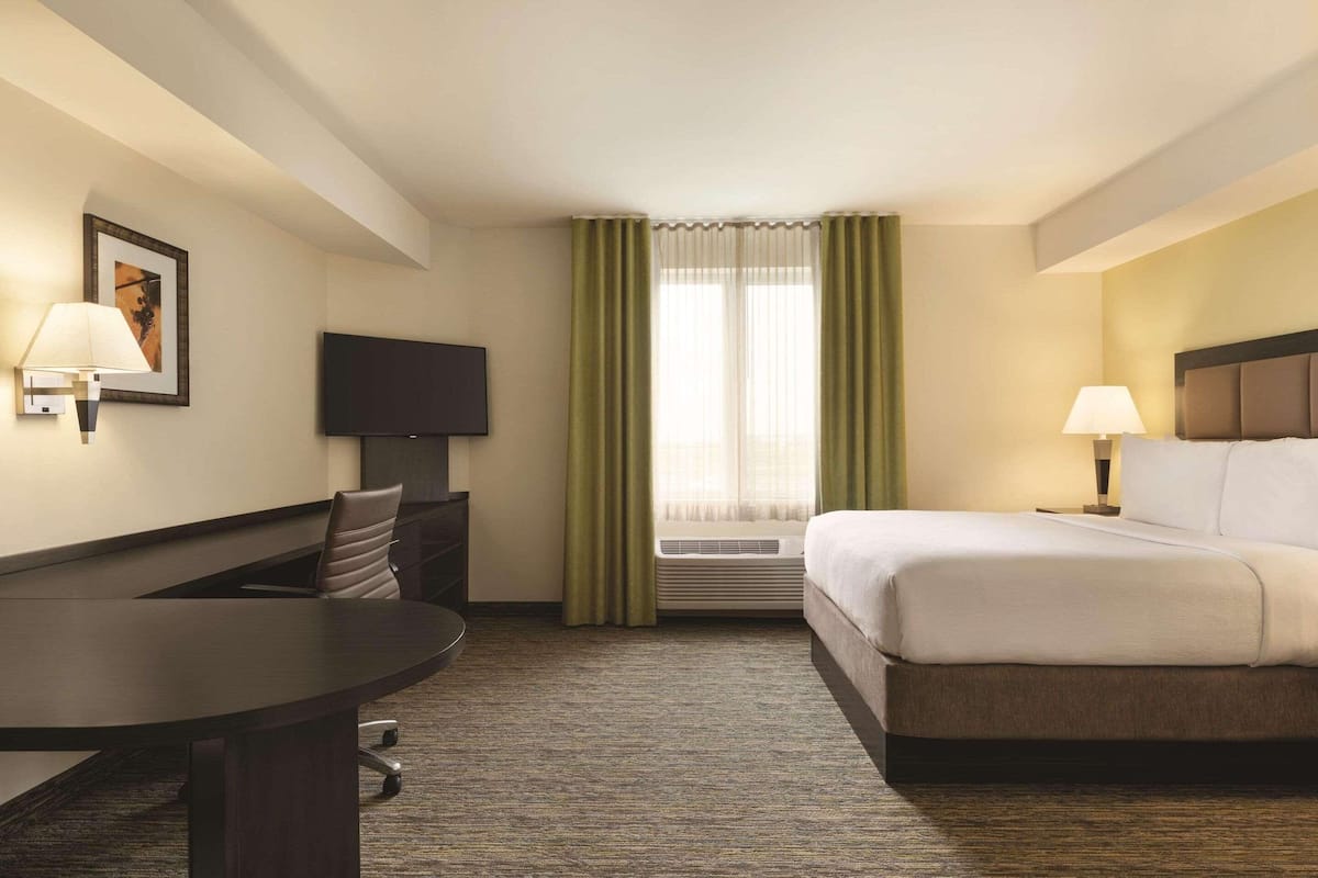 A hotel room with a bed, a desk, a chair, a television, and a window with curtains.