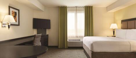 A hotel room with a bed, a desk, a chair, a television, and a window with curtains.
