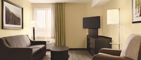 Una habitación de hotel con un sofá, una mesita redonda pequeña, un televisor y una lámpara.