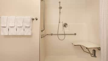 Zona de ducha con barra de apoyo, cabezal de ducha manual y asiento.