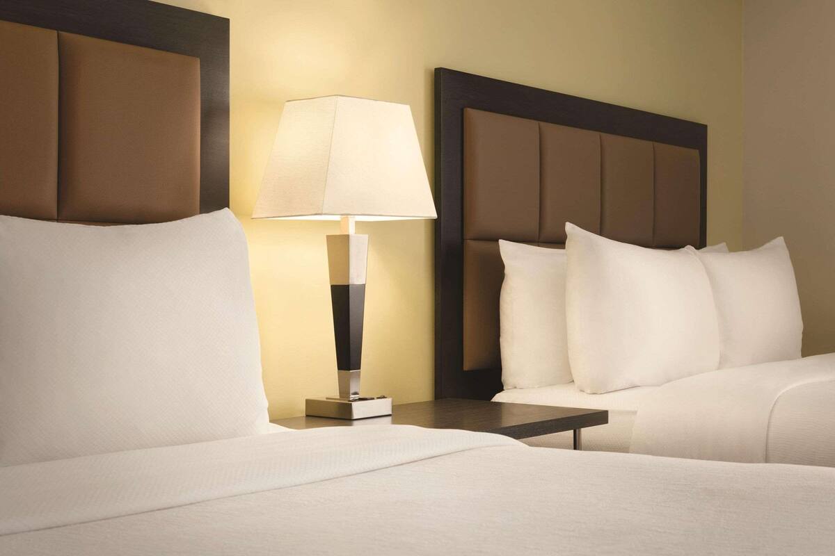 A hotel room with two beds, a nightstand with a lamp, and a headboard with a dark frame.