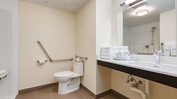 A modern bathroom with a toilet, handrails, a sink with toiletries, and a mirror.