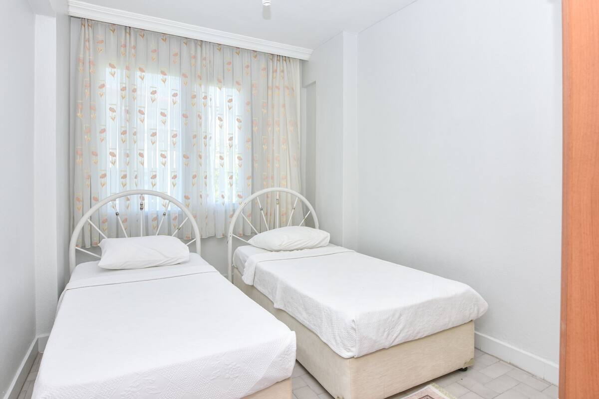 A bedroom with two single beds, white bedding, and a window with floral curtains.