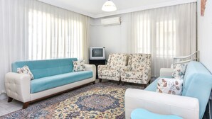 Una sala de estar con un sofá, dos sillones, un televisor y una alfombra estampada.