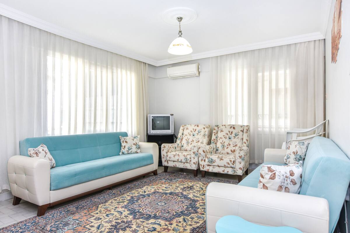 A living room with a sofa, two armchairs, a television, and a patterned rug.
