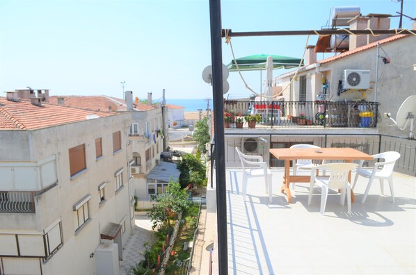 A balcony with a table and chairs, overlooking a street with buildings and a clear sky. - Yade Apart Pansiyon (Ayvalik)