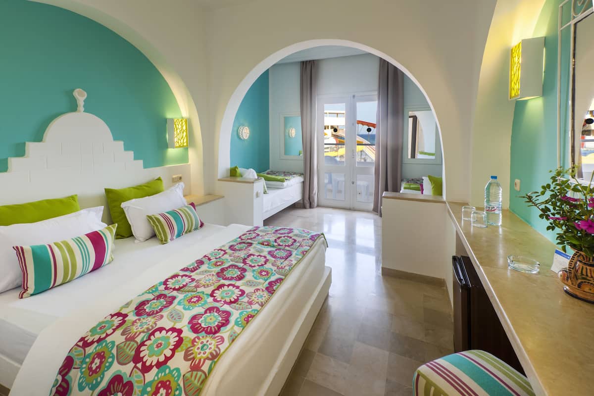 A hotel room with a large bed, a desk, and a view of the pool area.