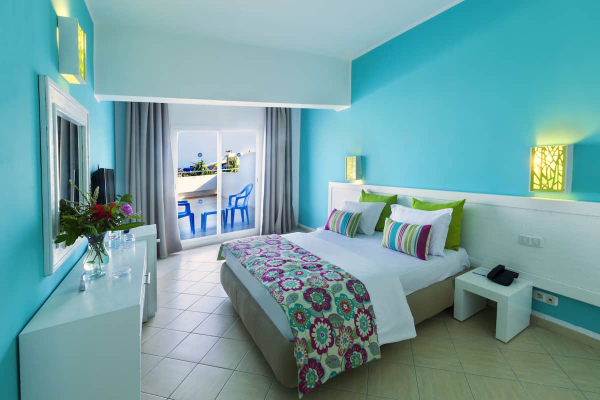 A hotel room with a bed, bedside table, and a view of the outside balcony.