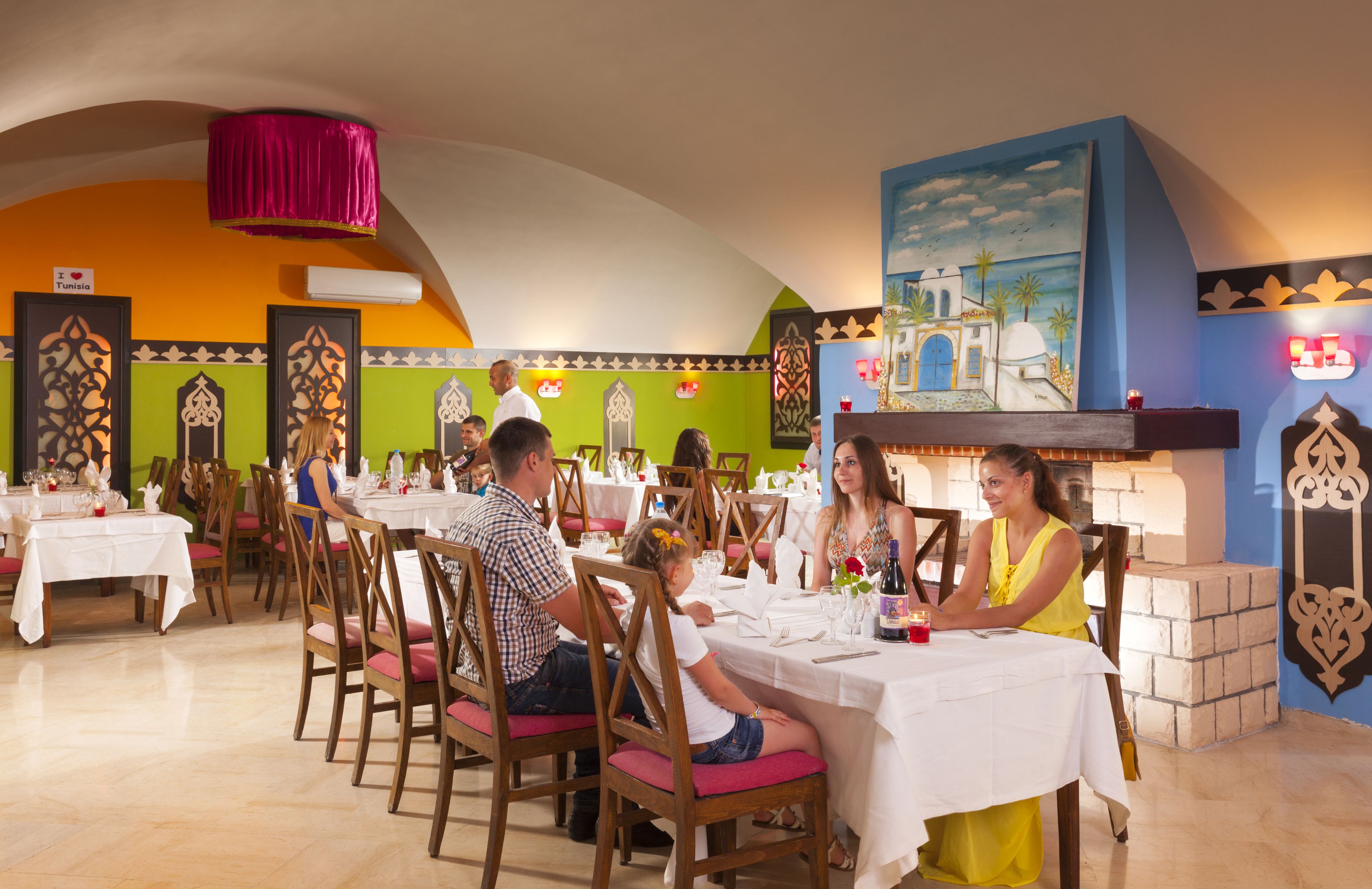 A restaurant with multiple tables and chairs, a decorative ceiling, and a mural on the wall.