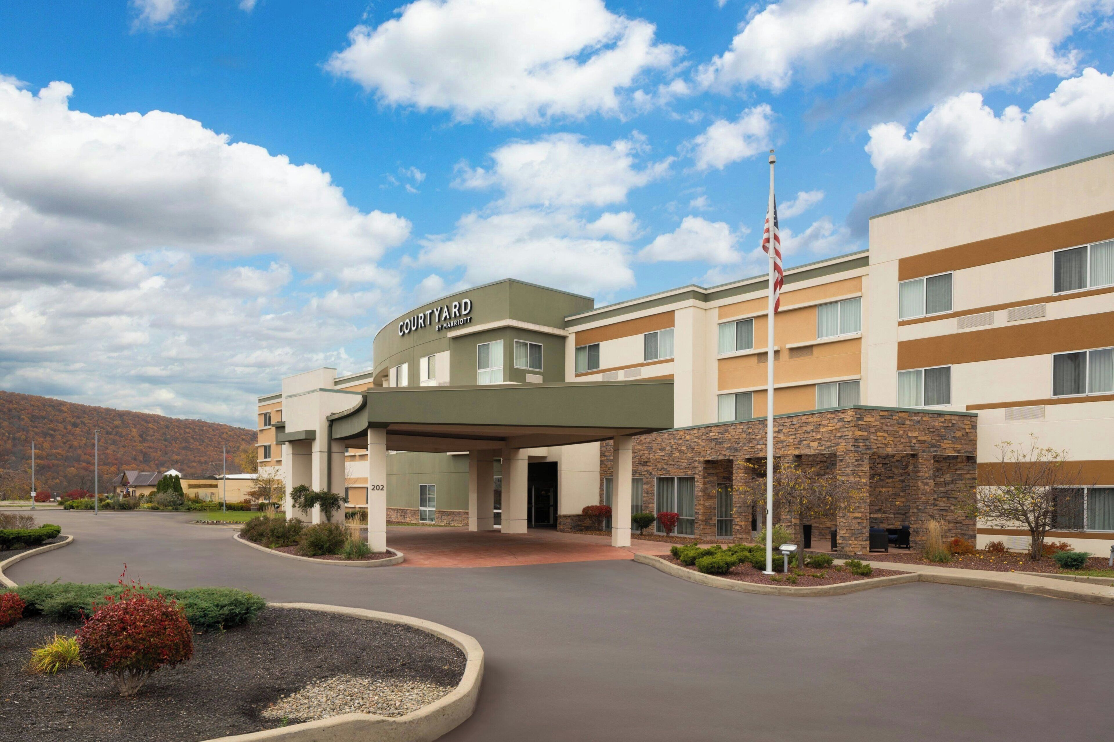 A Courtyard by Marriott hotel with a covered entrance, a parking lot, and a mountainous backdrop.