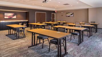 A conference room with multiple tables and chairs, a projector, and a carpeted floor.