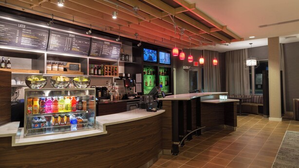 A modern bar area with a wooden counter, a beverage dispenser, and a menu board. - Courtyard by Marriott Elmira Horseheads (Horseheads)