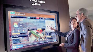 A large digital display at a Courtyard Marriott hotel, featuring a GoBoard interface with local news, weather, and market information.