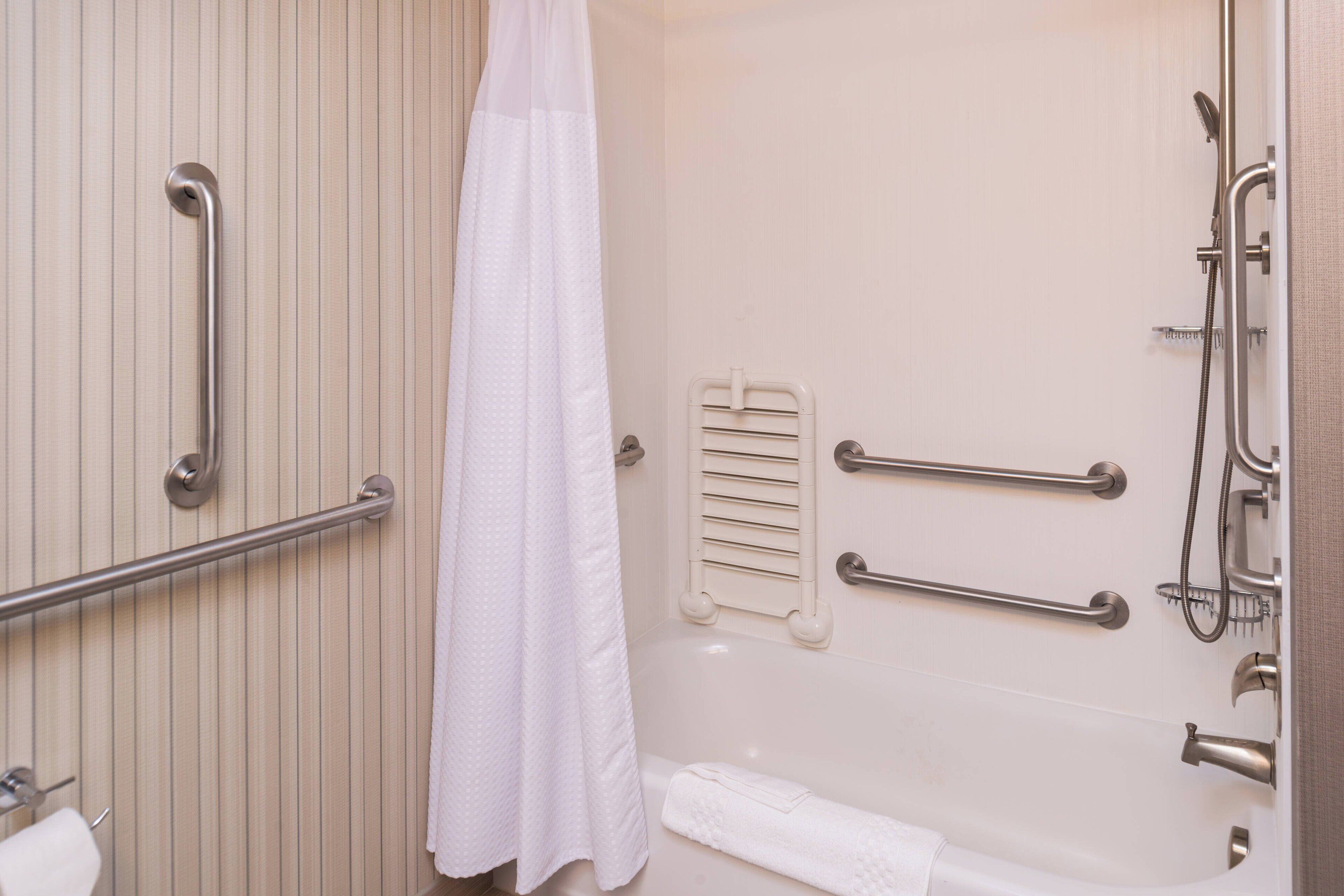 A bathroom with a bathtub, a shower, and handrails.