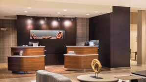 A modern reception area with two reception desks, a large abstract painting, and a seating area with a round table and chairs. - Courtyard by Marriott Elmira Horseheads (Horseheads)