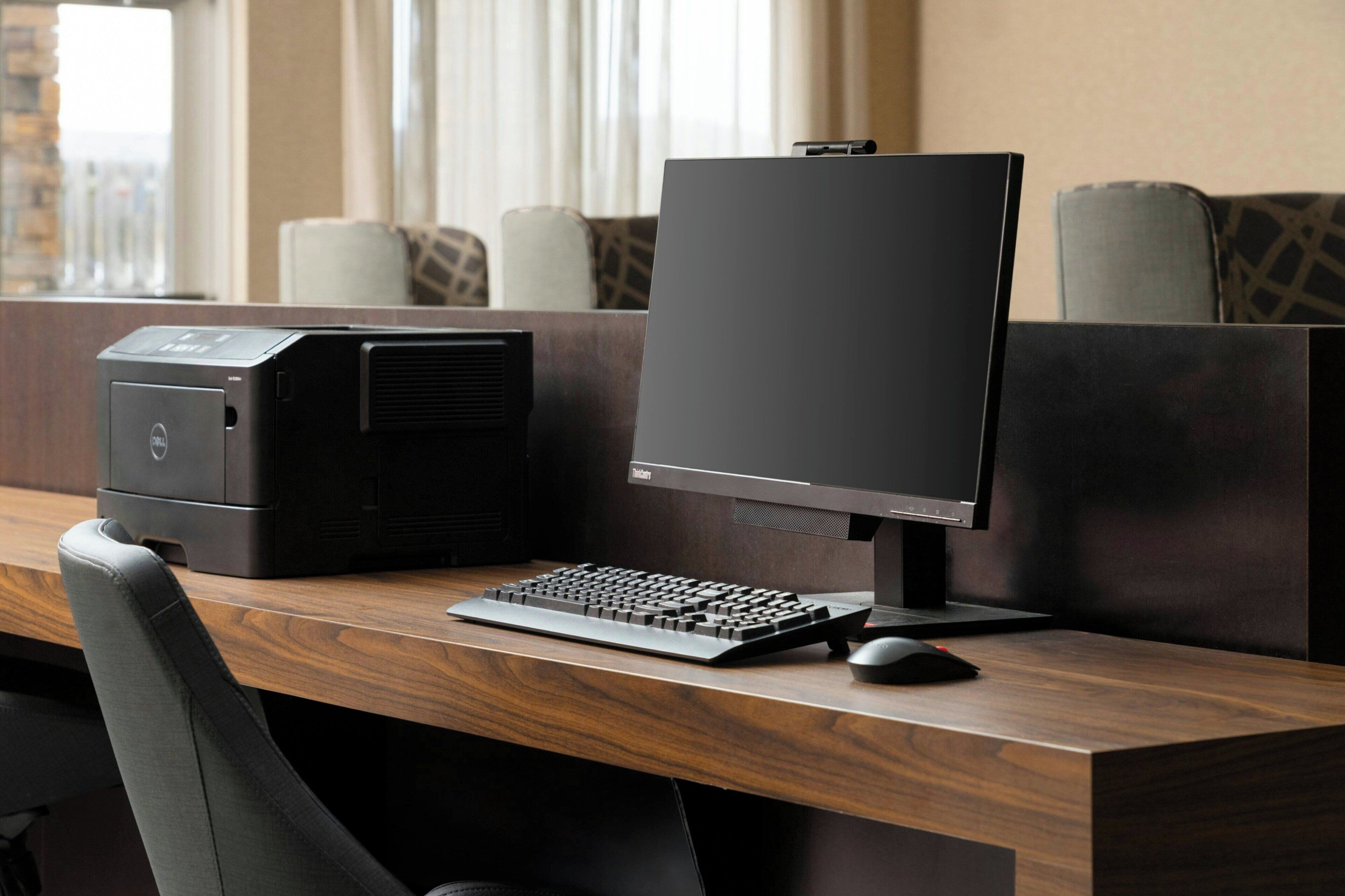 Un'area di lavoro in hotel con un computer desktop, tastiera e mouse su una scrivania in legno.