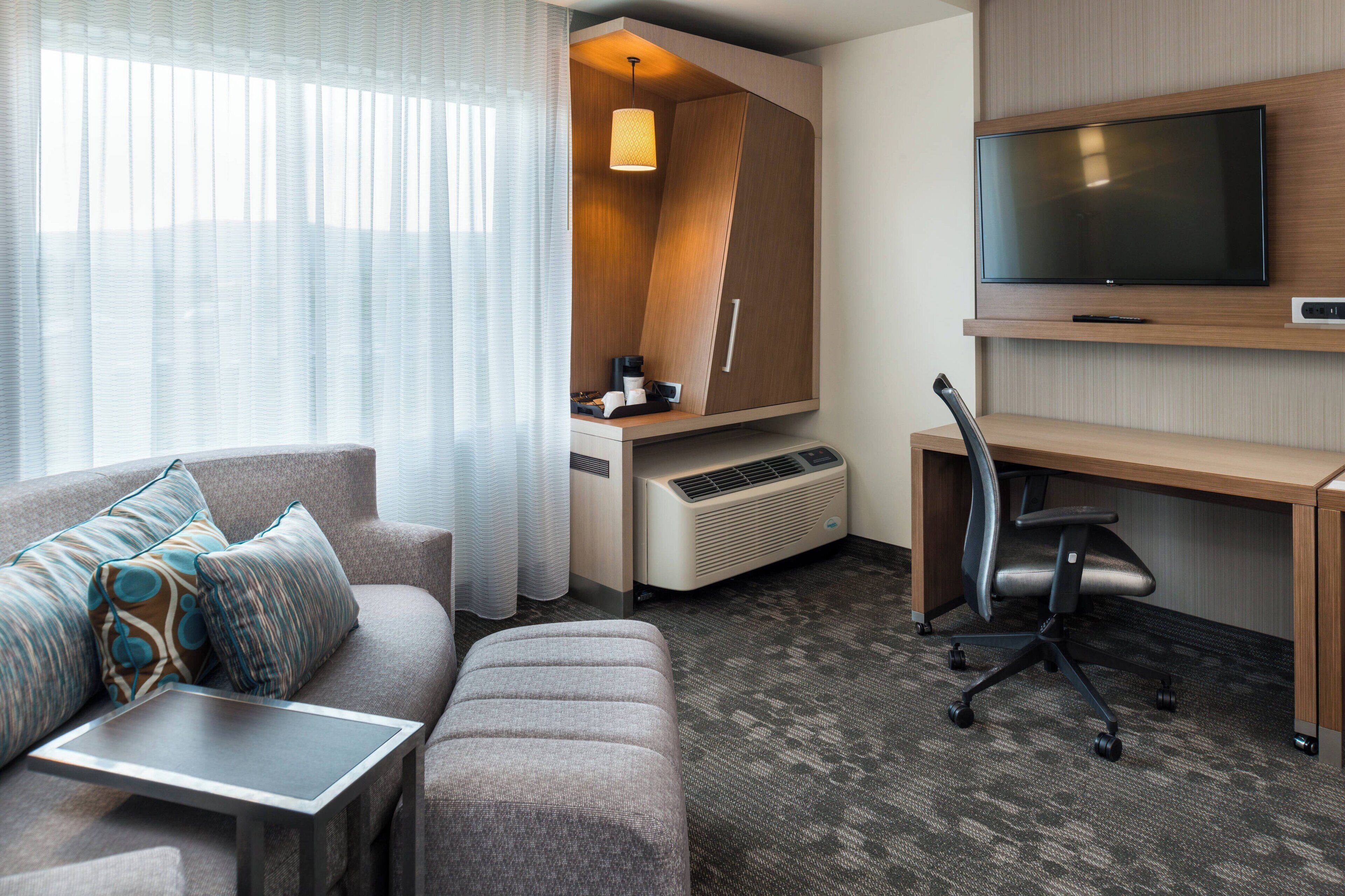 Ein Hotelzimmer mit Sofa, Schreibtisch, Fernseher und integriertem Heizkörper.