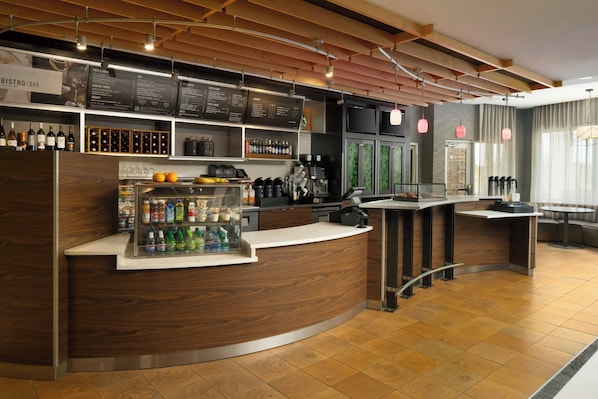 Un espace bar moderne avec un comptoir en bois incurvé, un assortiment de boissons en bouteille et un tableau affichant le menu au-dessus.