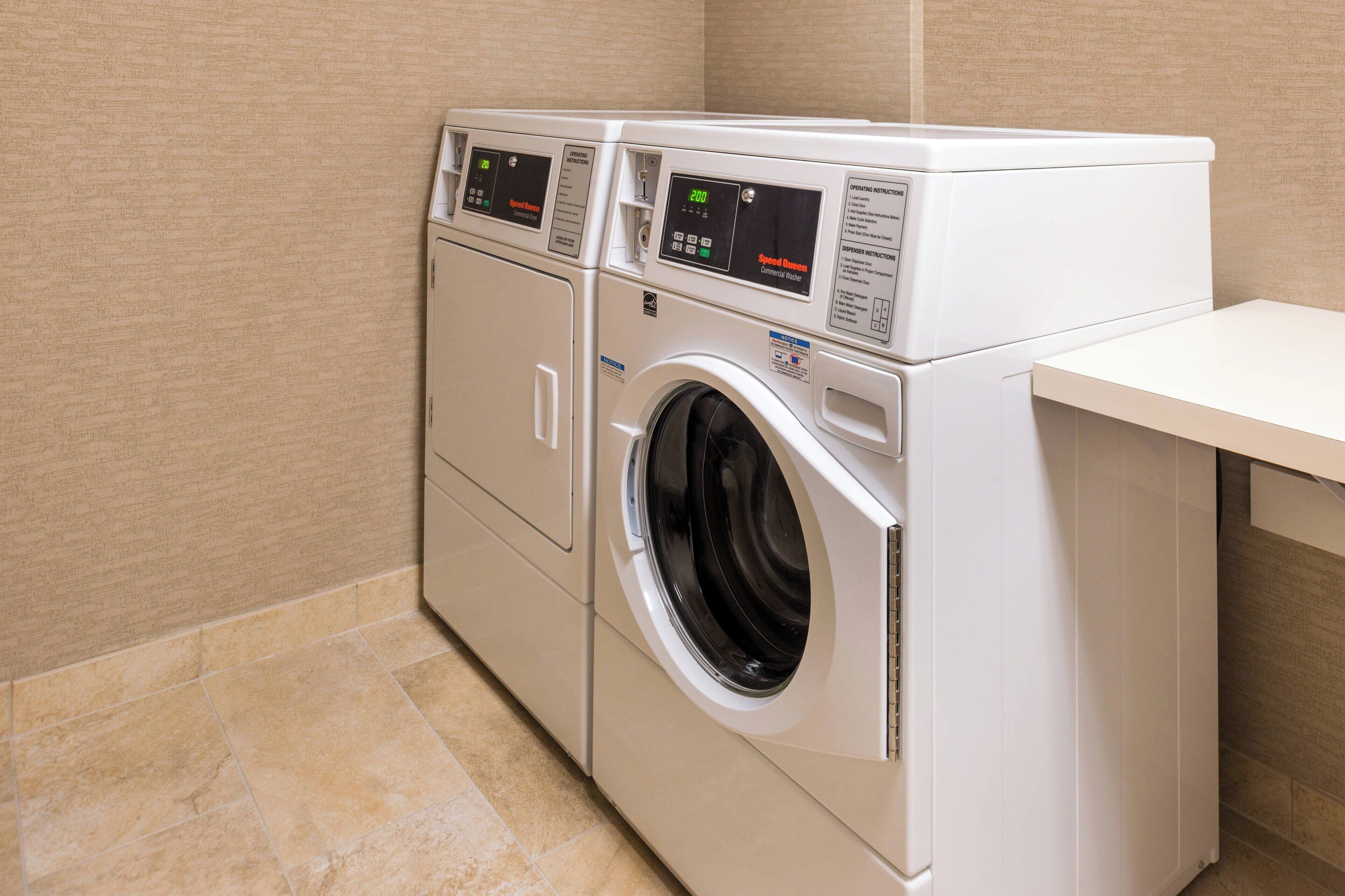 A front-loading washing machine with a digital control panel, a stainless steel door, and a beige tiled floor.